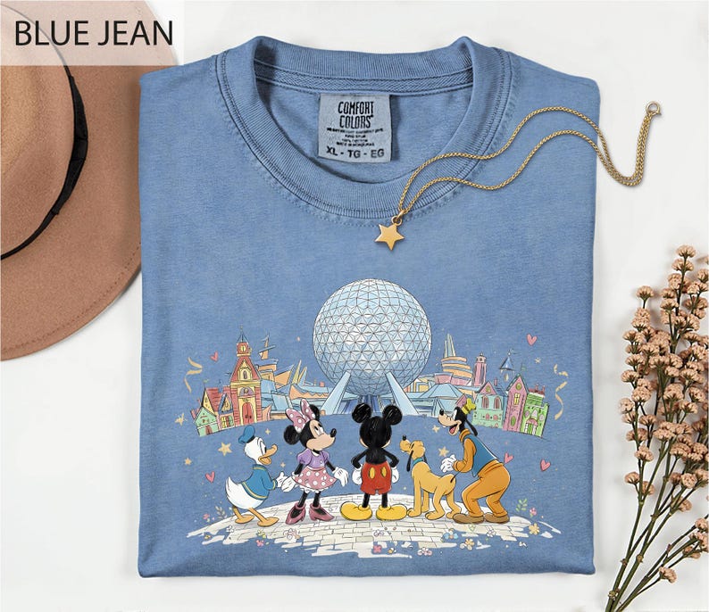A blue t-shirt with a graphic of Disney characters Mickey Mouse, Minnie Mouse, Donald Duck, and Goofy, along with a large globe, is displayed on a white surface.