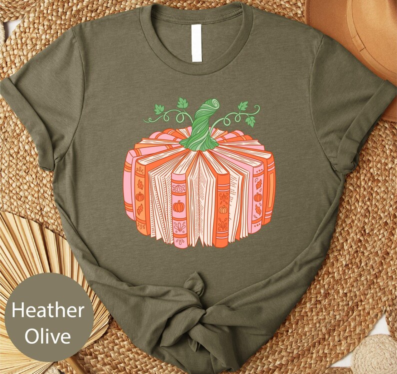 A t-shirt with a graphic design of a pumpkin made up of books, placed on a woven mat.
