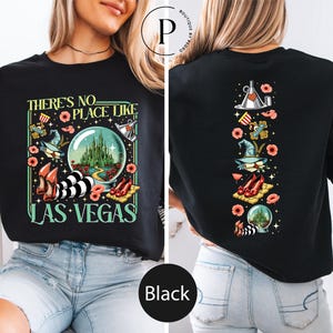 May include: Black sweatshirt with a colorful graphic design. The front features the text "THERE'S NO PLACE LIKE LAS VEGAS" with images of a crystal ball, red shoes, and a witch's hat. The back has a vertical design with similar elements.