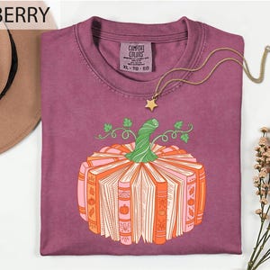 a purple t-shirt with a pumpkin graphic and a necklace, along with a hat and some flowers.