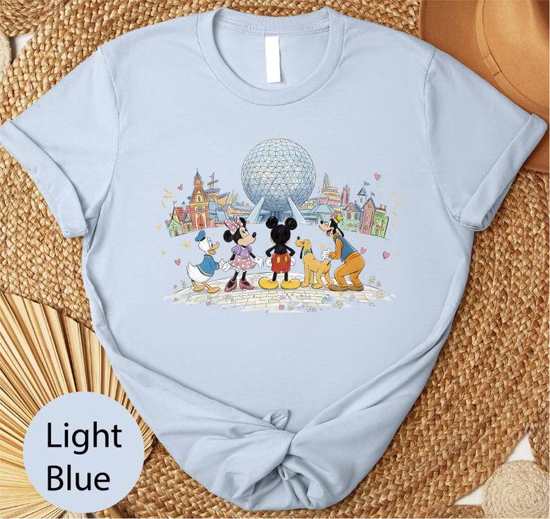 A light blue t-shirt with a graphic design featuring Disney characters Mickey Mouse, Minnie Mouse, Donald Duck, and Goofy standing in front of the Earth's Fair Park attraction.