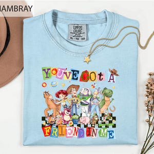 a light blue t-shirt with a colorful graphic design of characters from the Toy Story movie, along with the text "You've Got a Friend in Me".