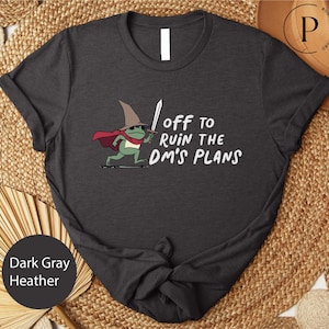 A black t-shirt with a graphic design depicting a frog wearing a wizard's hat and holding a sword, along with the text "Off to ruin the dm's plans".