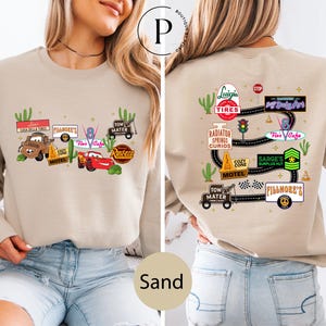 a woman wearing a beige sweater with various car-related logos and illustrations on the front and back.