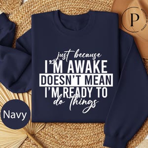 May include: Navy blue sweatshirt with the text "just because I'm awake doesn't mean I'm ready to do things" in white. The sweatshirt is a crew neck style.