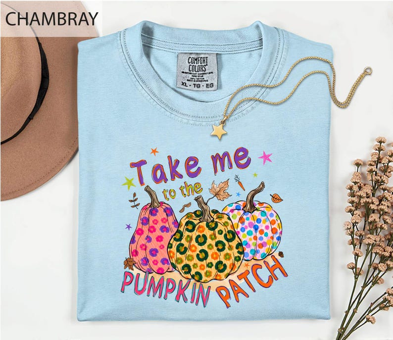 a light blue t-shirt with a colorful graphic design of three spotted pumpkins and the text "Take me to the pumpkin patch" printed on it.