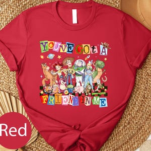 A red t-shirt with a colorful graphic design featuring characters from the Toy Story franchise, including Woody, Buzz Lightyear, and other beloved characters.