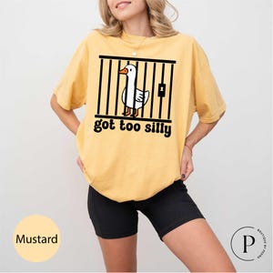 Peut inclure: T-shirt moutarde avec un dessin d'oie derri&egrave;re des barreaux et le texte "got too silly". Le t-shirt est de coupe ample, et la couleur est &eacute;tiquet&eacute;e "Mustard".
