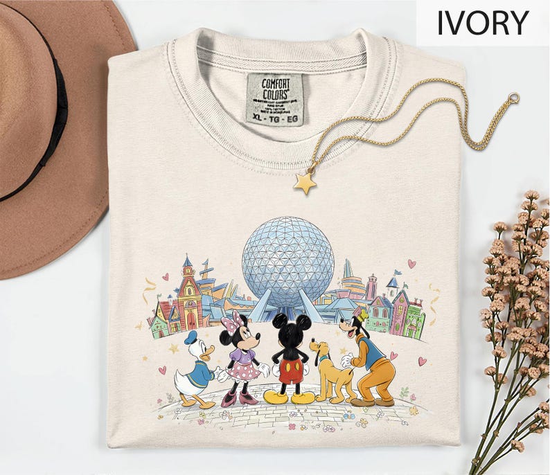 A white t-shirt with a Disney-themed graphic of Mickey Mouse, Minnie Mouse, Goofy, and Donald Duck standing in front of the Earth's Fairground, with a globe and various landmarks in the background.
