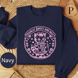 A navy blue sweatshirt with a pink graphic design on it, featuring a cat and the text "Usually Sweet and Nice BUT FUCK ICE".