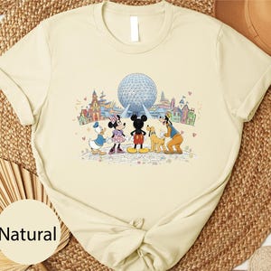 A t-shirt with a cartoon image of Disney characters, including Minnie Mouse, Donald Duck, Goofy, and Mickey Mouse, standing in front of the Earth's observation deck at Walt Disney World.