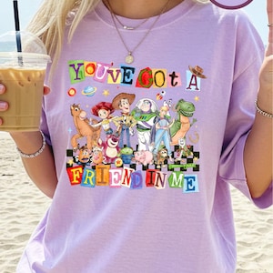 A woman wearing a purple t-shirt with a colorful graphic of characters from the Toy Story movie, including Woody, Buzz Lightyear, and other beloved characters.