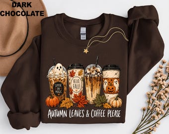 May include: A dark chocolate brown crewneck sweatshirt featuring a graphic of four coffee cups surrounded by autumn leaves and pumpkins. The cups display text reading Sippin on Magic, Hello Fall, and Autumn Leaves & Coffee Please in white lettering.