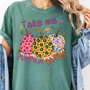 A woman wearing a green t-shirt with a graphic design of three colorful pumpkins and the text "Take me to the pumpkin patch" printed on it.
