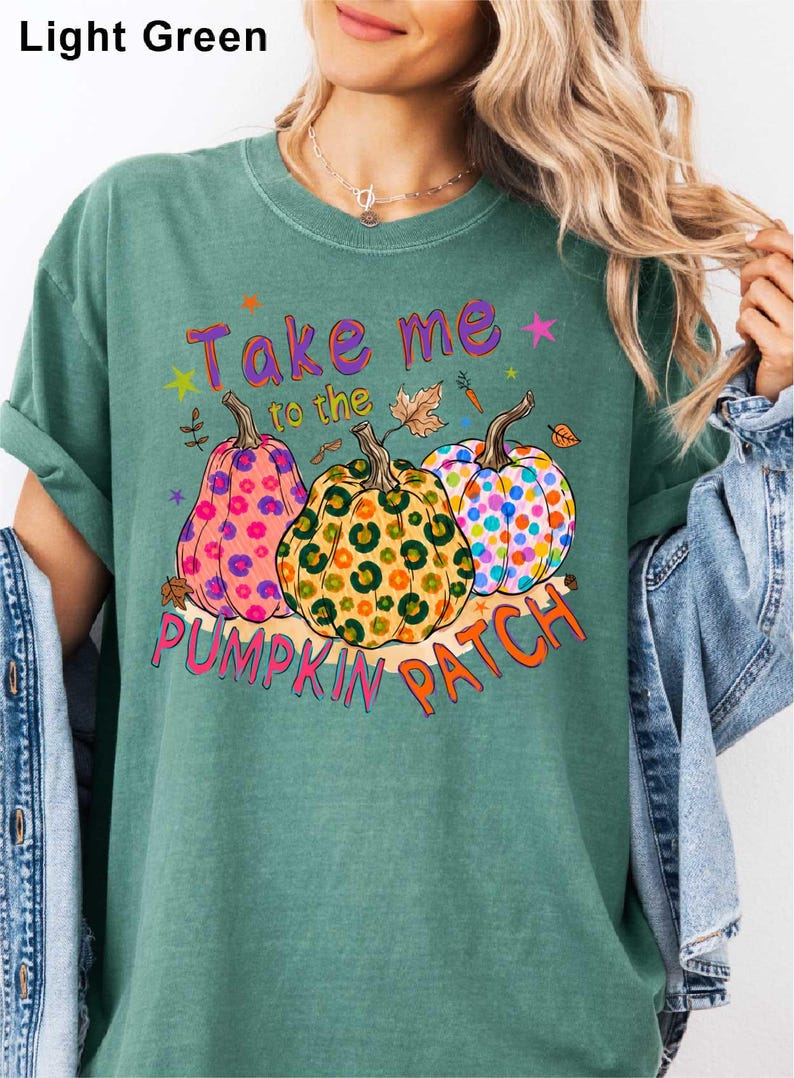 A woman wearing a green t-shirt with a graphic design of three colorful pumpkins and the text "Take me to the pumpkin patch" printed on it.
