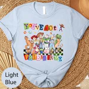 A light blue t-shirt with a colorful graphic design featuring characters from the Toy Story movie, including Woody, Buzz Lightyear, and other beloved characters.