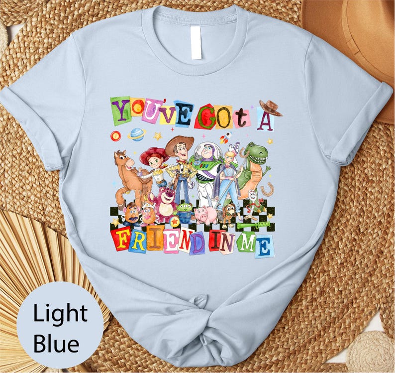 A light blue t-shirt with a colorful graphic design featuring characters from the Toy Story movie, including Woody, Buzz Lightyear, and other beloved characters.