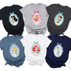 May include: Six different t-shirts featuring Disney princesses in a vintage-inspired design. Each shirt has a different princess in a pearl-encrusted frame with a blue ribbon. The princesses featured are Jasmine, Aurora, Snow White, Ariel, Alice, and Cinderella.
