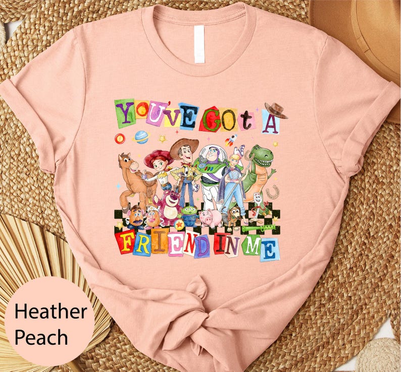 A pink t-shirt with a colorful graphic design featuring characters from the Toy Story movie, including Woody, Buzz Lightyear, and other beloved characters.