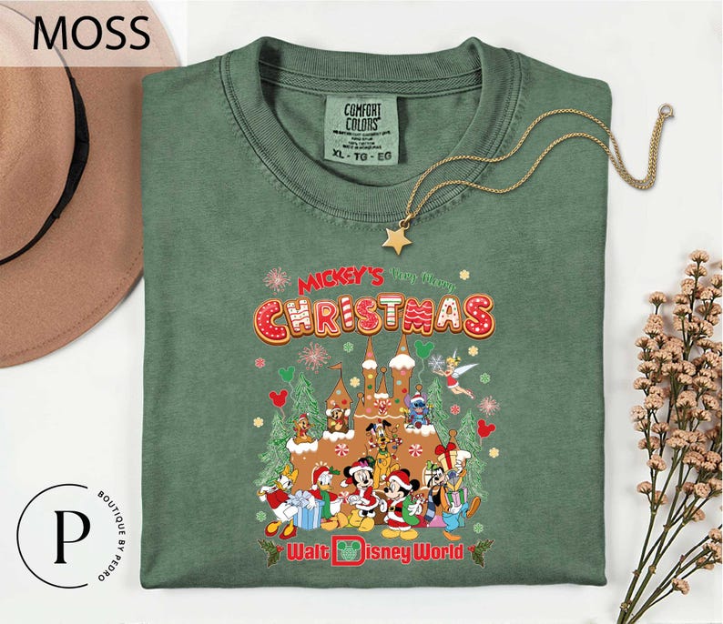 A green t-shirt with a Christmas-themed graphic design, including various Disney characters and holiday decorations, is displayed on a white background.