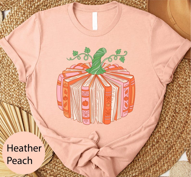 A pink t-shirt with a graphic design of a pumpkin made up of books, surrounded by leaves and vines.