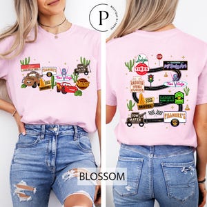 A woman wearing a pink t-shirt with various car-related graphics and text, including a pink car, a pink car with a tire, and a pink car with a tire.