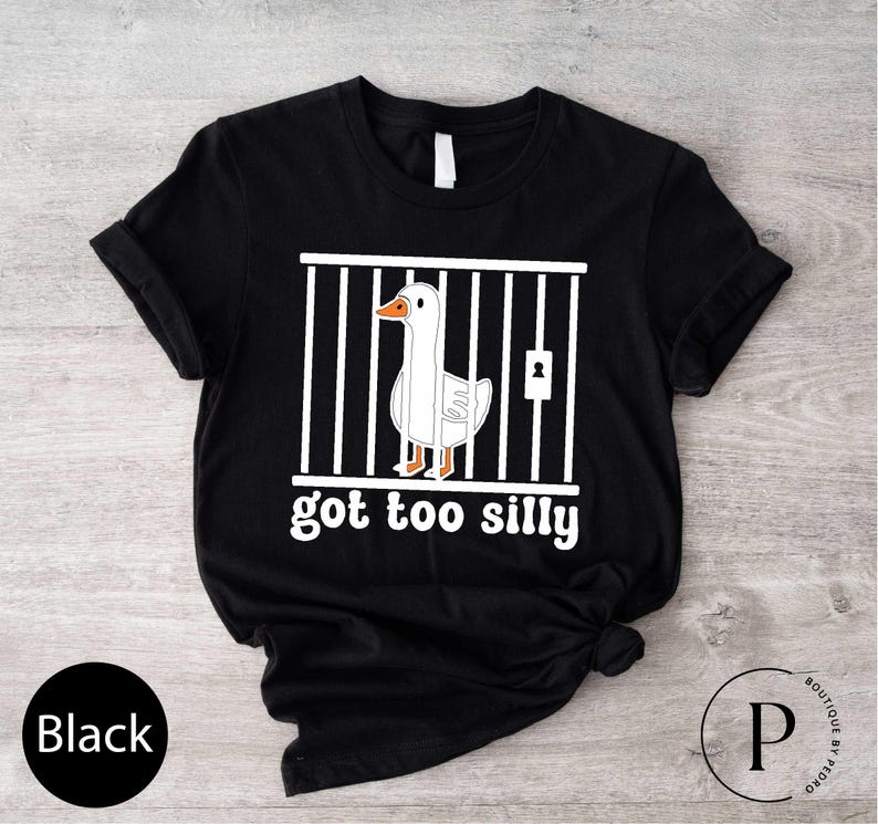 Peut inclure: T-shirt noir avec un dessin d'oie en cage et le texte "got too silly" en blanc. L'oie est blanche avec un bec et des pattes oranges. Le t-shirt a un col rond et des manches courtes.