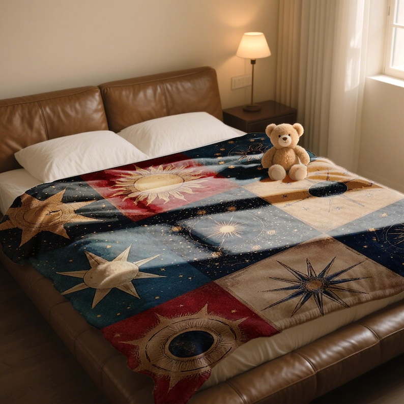 May include: A colorful throw blanket with a celestial design featuring suns, stars, and geometric patterns in shades of red, blue, and beige. The blanket is displayed on a bed with a brown leather headboard.