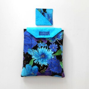 May include: A quilted fabric case and matching coaster. The case features a black background with blue floral patterns, a turquoise flap with a rhinestone embellishment, and a turquoise coaster with a floral design. The case is approximately 9 inches tall.