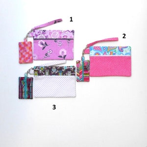 May include: Three fabric wristlet pouches with matching keychains. One pouch is pink with a floral pattern, another is hot pink with a polka dot pattern, and the third is white with a polka dot pattern and owl design.