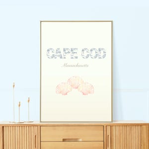 Peut inclure: Une affiche blanche avec le texte "CAPE COD Massachusetts" en lettres bleues et grises. L'affiche présente trois coquillages roses et blancs.