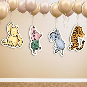 May include: Four Winnie the Pooh character cutouts hanging from gold balloons. The characters are Winnie the Pooh, Piglet, Eeyore, and Tigger.
