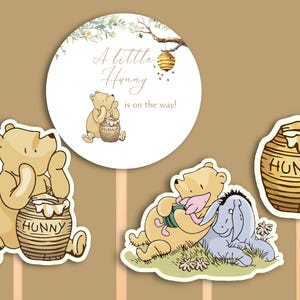 May include: Three Winnie the Pooh themed cake toppers. One round topper with a beehive and the text "A little Hunny is on the way!" Another topper features Winnie the Pooh holding a honey pot. The third topper shows Winnie the Pooh and Piglet sitting together.