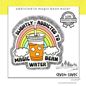 May include: A silver glitter sticker with a rainbow and a cup of iced coffee. The sticker says "Slightly Addicted to Magic Bean Water".