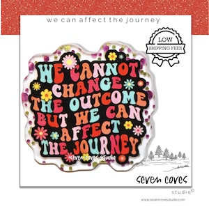 May include: A clear, irregular-shaped sticker with the text "WE CANNOT CHANGE THE OUTCOME BUT WE CAN AFFECT THE JOURNEY" in colorful, retro-style lettering. The sticker has a glittery border and floral accents. The words "seven coves studio" are also visible.