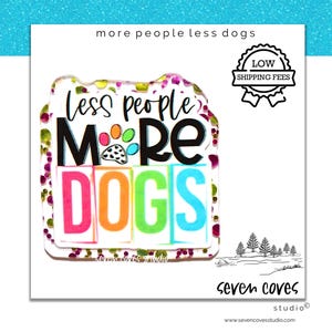 May include: A colorful, glittery sign with the text "Less people More DOGS" in a rainbow font. The sign is surrounded by a white border and has a paw print in the middle of the word "More".
