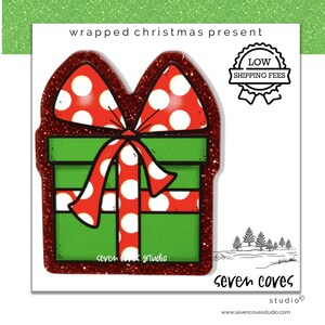 May include: A festive Christmas gift illustration with a green box, red polka-dot bow, and glittery red outline. The image includes the text "wrapped christmas present" and "seven coves studio".