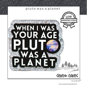 May include: A black and silver glittery pin with the text "WHEN I WAS YOUR AGE PLUTO WAS A PLANET". The pin features a colorful planet graphic and the words "seven coves studio".