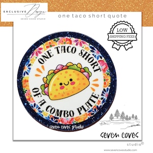 May include: A round, white plate with a blue floral border and the text "ONE TACO SHORT OF A COMBO PLATE." A cartoon taco with a smiling face is in the center. The plate has the words "seven coves studio" at the bottom.