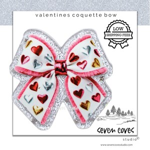 May include: A Valentine's Day-themed coquette bow with a white base, adorned with red, silver, and gold hearts. The bow has a pink trim and a glittery border. The text "valentines coquette bow" is at the top.