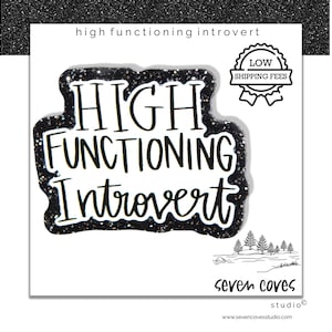 May include: A white card with the phrase "HIGH FUNCTIONING Introvert" in black, glitter-outlined letters. The card also features a "LOW SHIPPING FEES" badge and a small illustration of trees. The Seven Coves Studio logo is at the bottom.