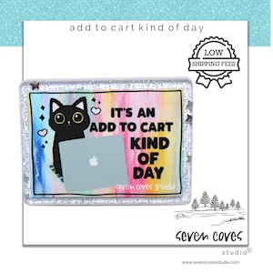 May include: A rectangular sticker with a black cat holding a laptop, and the text "IT'S AN ADD TO CART KIND OF DAY." The background is a colorful blend of pink, yellow, and blue. The sticker has a glittery border.