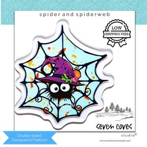 May include: A transparent flatback featuring a cartoon spider wearing a purple witch hat, set against a light blue spiderweb background. The design includes orange accents and the text "spider and spiderweb". The flatback is double-sided.