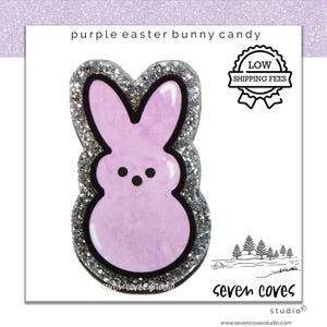 May include: A purple Easter bunny candy charm with a glittery silver border. The charm has a light purple body, black eyes, and a black outline. The text "purple easter bunny candy" is at the top.