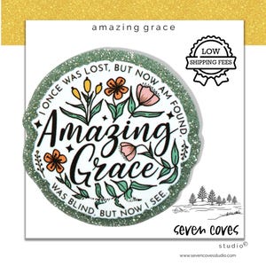 May include: A round sticker with the words "Amazing Grace" in a decorative font, surrounded by floral illustrations in orange, pink, and green. The sticker has a glittery green border and the text "I once was lost, but now I am found. Was blind, but now I see."