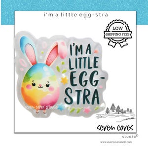 May include: A colorful Easter-themed sticker with the text "I'm a little egg-stra." The design features a cartoon egg with bunny ears and a smiling face, surrounded by stars and floral accents. The sticker also includes the "seven coves studio" logo.