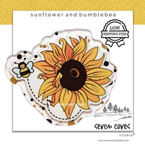 May include: A clear acrylic charm featuring a yellow sunflower and a small bumblebee with black and yellow stripes. The design includes black polka dots and gold accents on a transparent background. The text sunflower and bumblebee is visible.