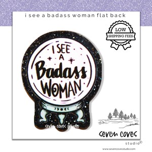 May include: A flat back pin with the text "I SEE A Badass WOMAN" inside a crystal ball design. The pin has a black glitter border and a white background. The pin also has a "LOW SHIPPING FEES" badge.
