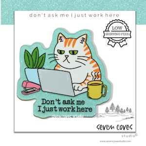 May include: A sticker featuring a grumpy cat working on a laptop, with the text "Don't ask me I just work here." The cat is orange and white, with a yellow mug and a plant. The sticker also has a "Low Shipping Fees" badge.