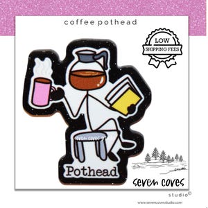 May include: A black enamel pin featuring a stick figure with a coffee pot for a head, sitting on a stool while holding a pink mug with steam and a yellow book. The text reads coffee pothead and Pothead, with a black background and glitter.